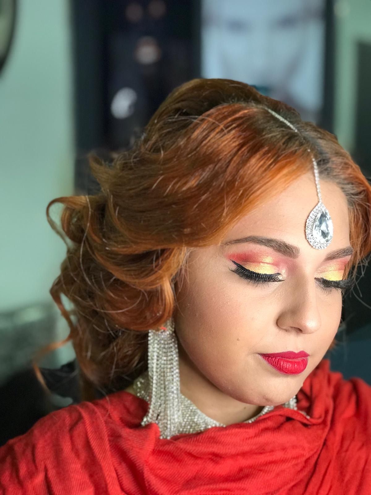 Mujer con cabello y maquillaje de color rojo vibrante, con joyas y una bufanda roja; ojos cerrados.