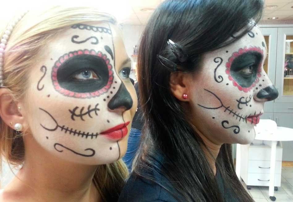 Dos mujeres con maquillaje de calavera del Día de Muertos, una al lado de la otra. Detalles de maquillaje negro, blanco y rojo en los rostros.
