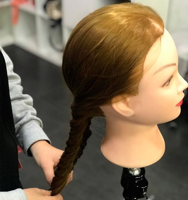 Cabeza de maniquí con cabello castaño peinado con una trenza de cola de pez. Una persona sujeta la trenza con sus manos.