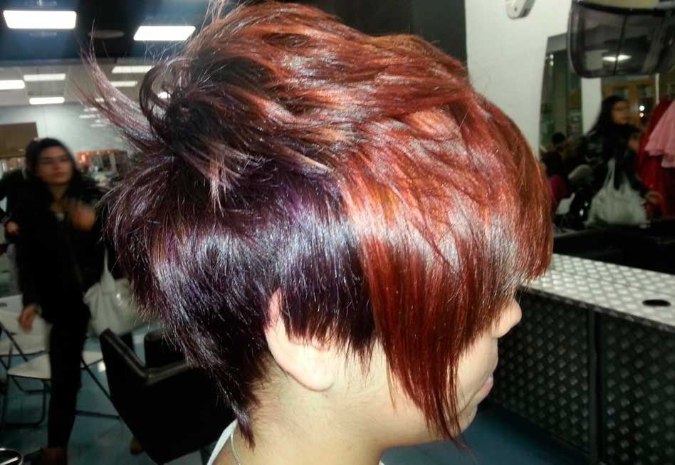 Mujer con cabello corto en capas en tonos rojos y morados en un salón de belleza.