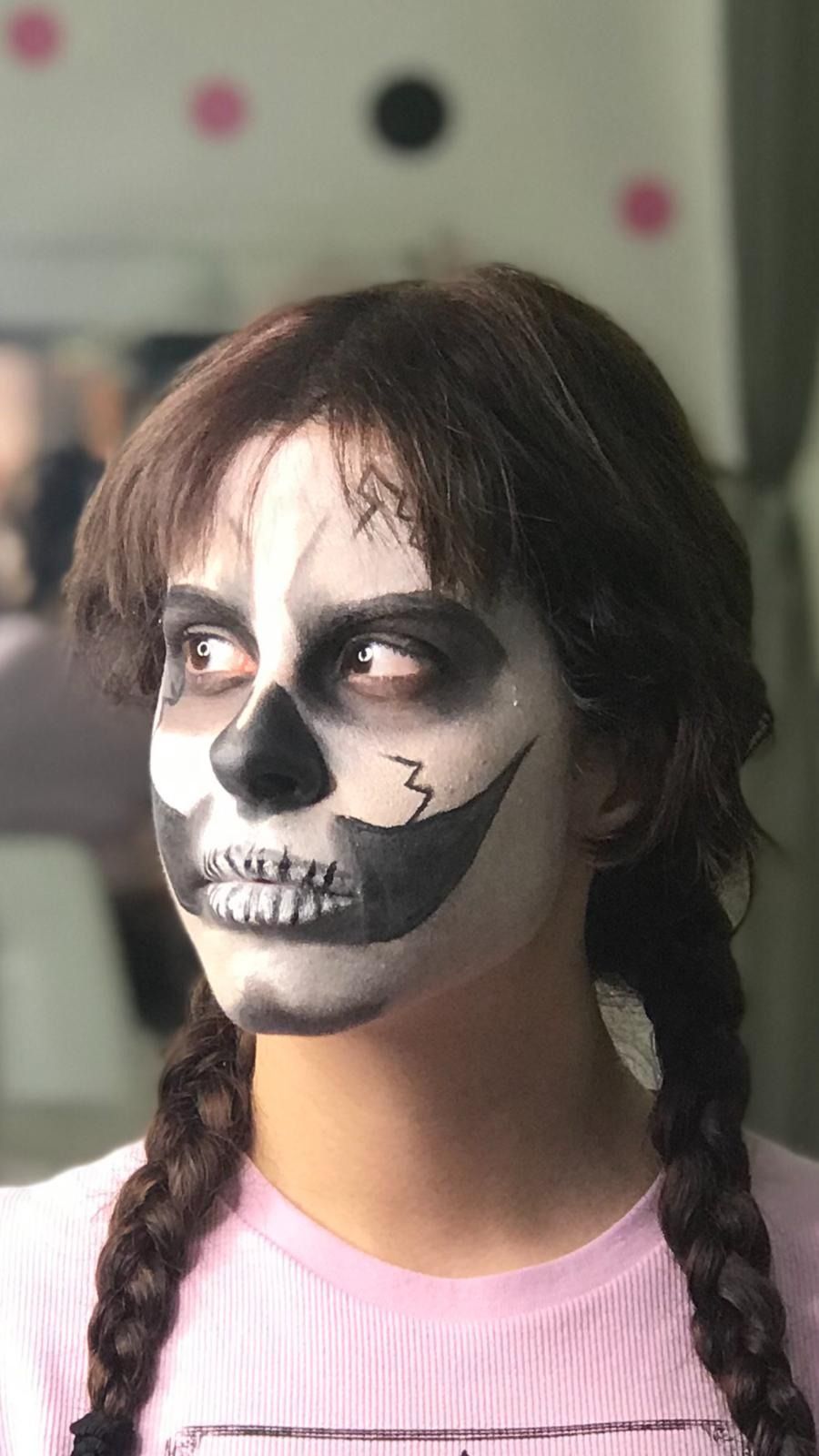 Chica con cara de calavera pintada, trenzas oscuras, mirando hacia un lado.