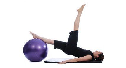 Mujer haciendo Pilates con pelota de ejercicios, piernas extendidas, sobre una colchoneta.