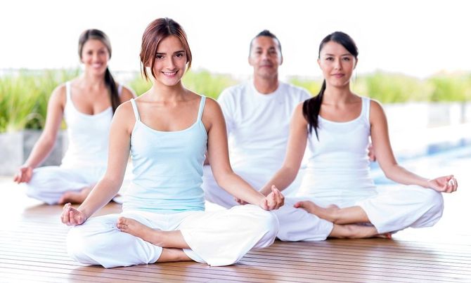 Grupo vestido de blanco meditando al aire libre en posición de loto.