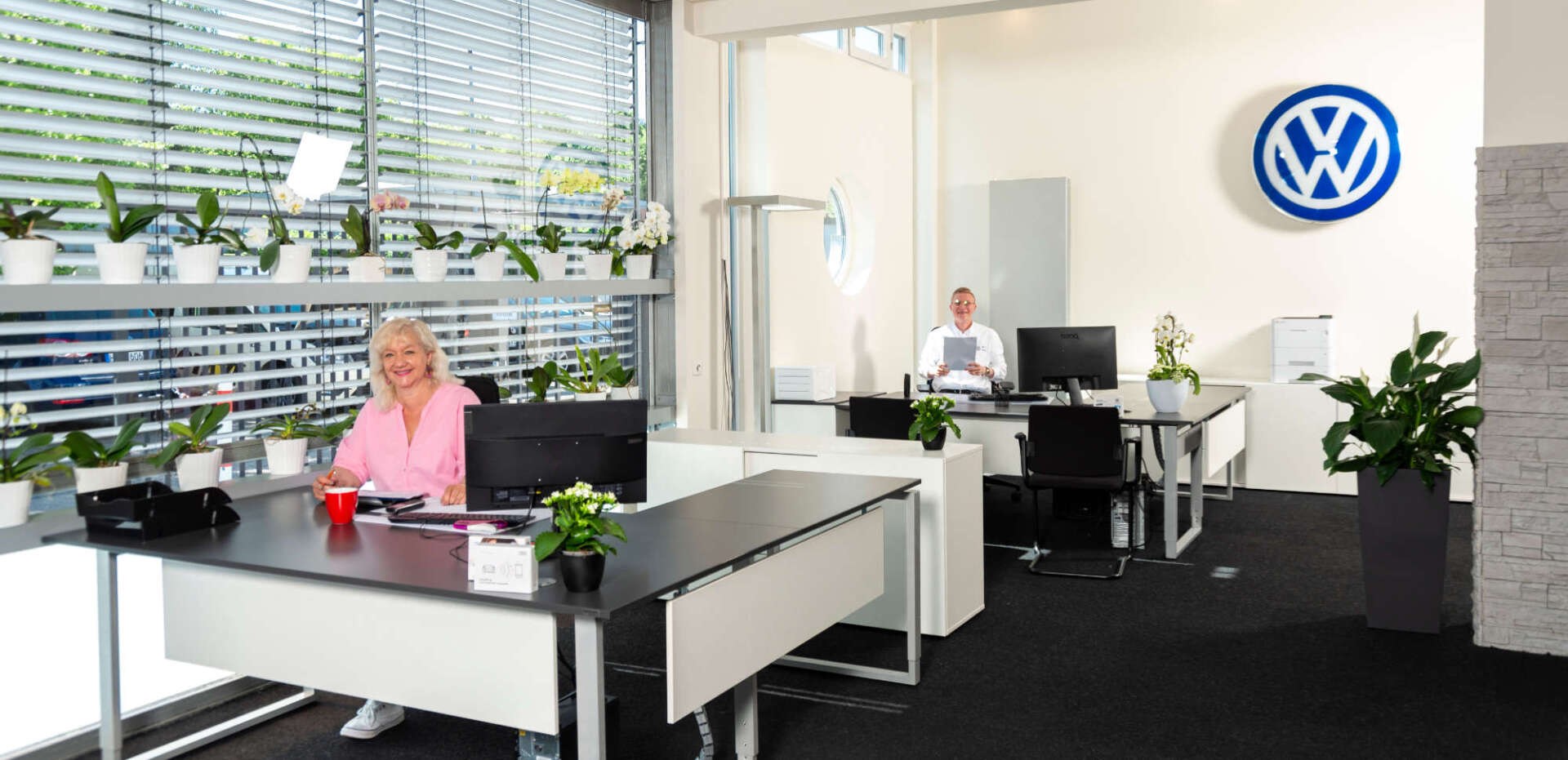 Eine Frau sitzt an einem Schreibtisch vor einem Volkswagen-Logo