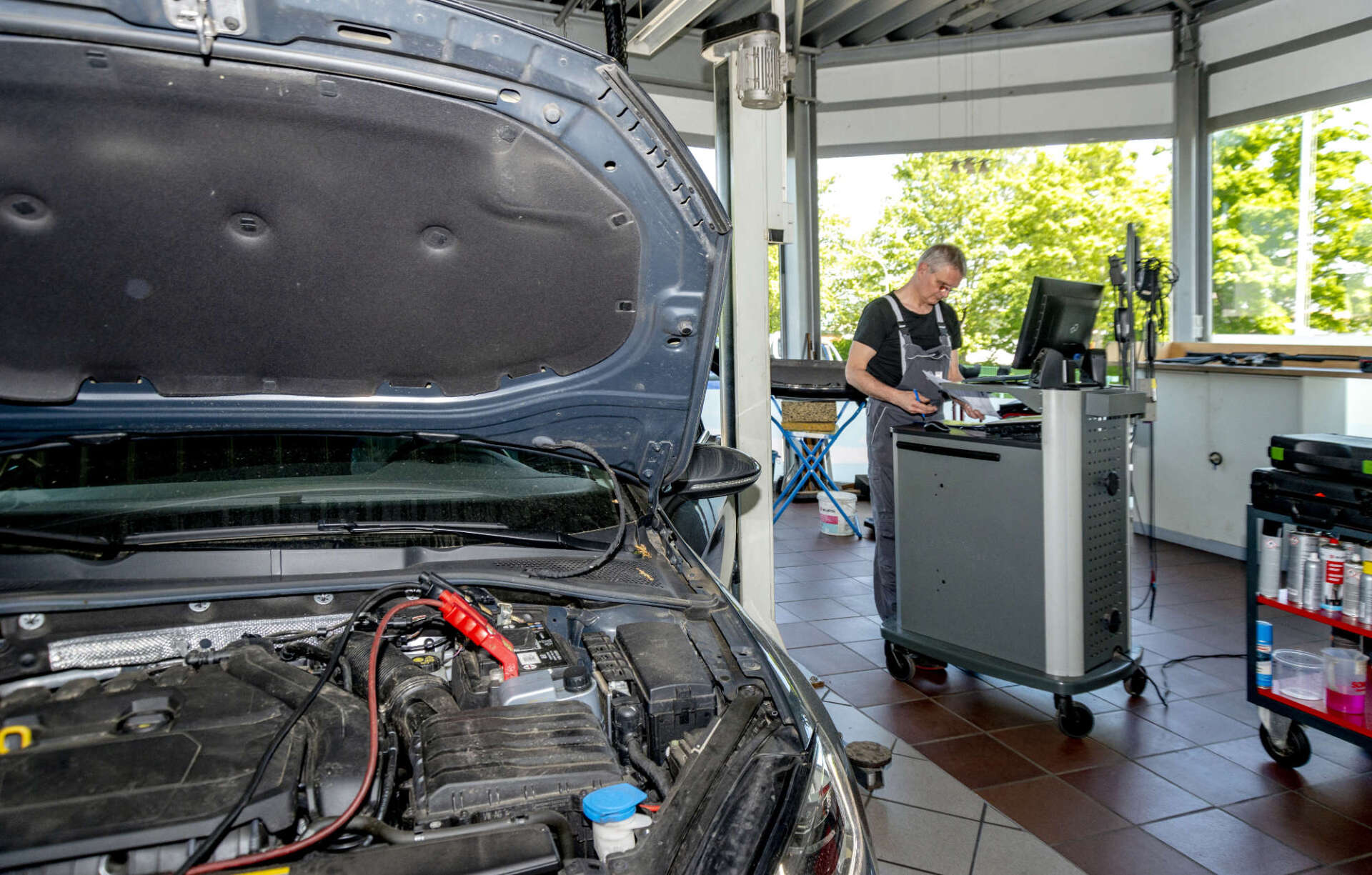 Ein Servicemitarbeiter arbeitet in einer Garage bei geöffneter Motorhaube an einem Auto