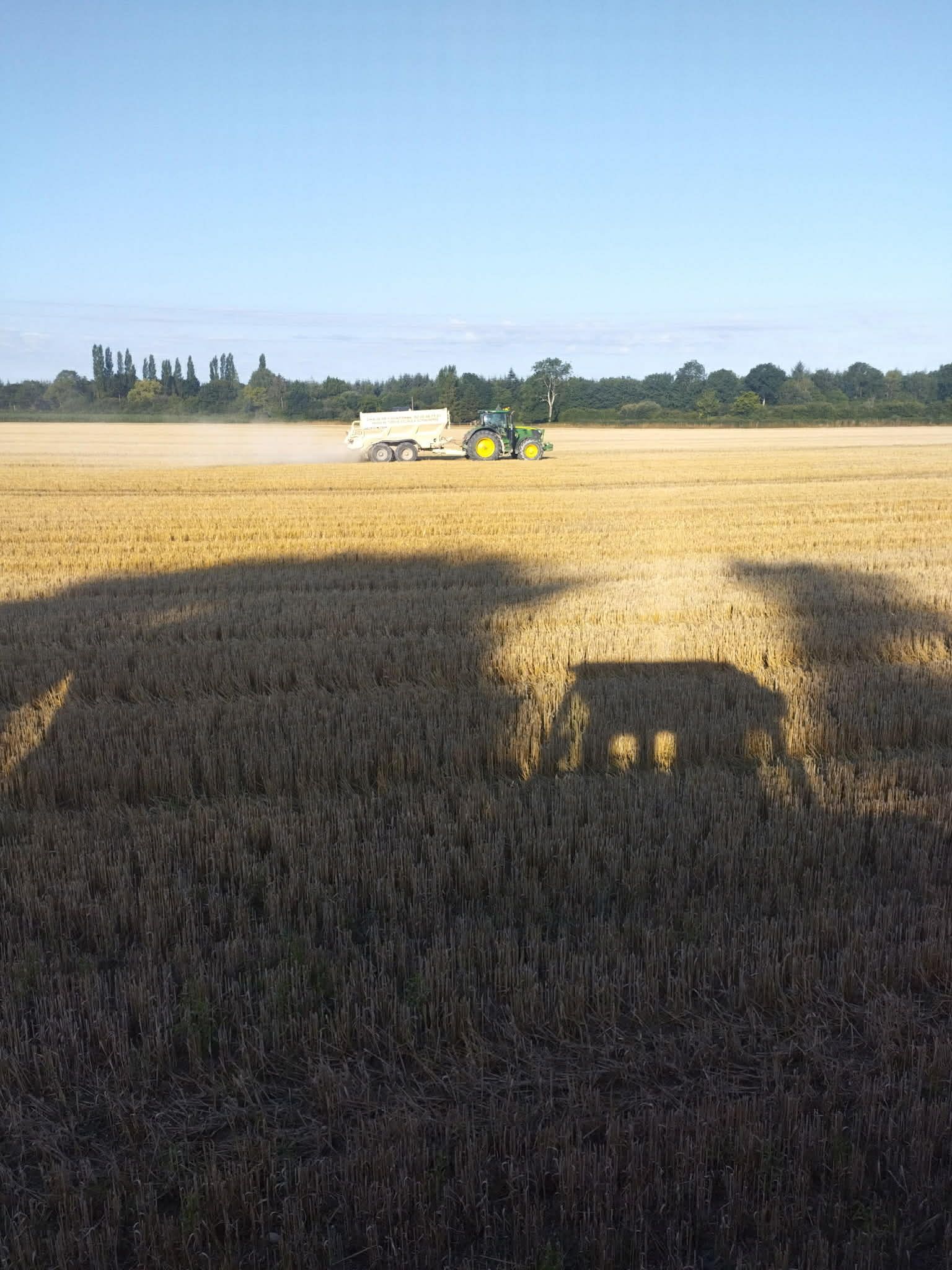 Un tracteur tirant du matériel agricole à travers un champ doré moissonné.
