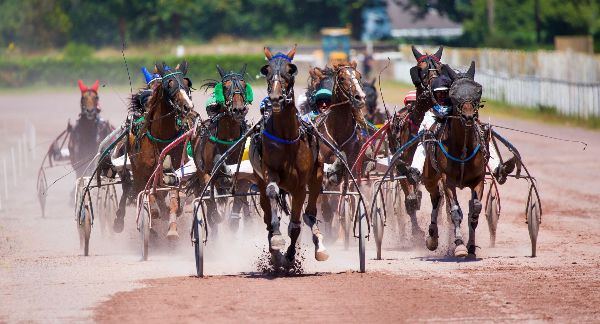 Un groupe de chevaux de course attelés, tirés par des conducteurs en sulkys, filant à toute allure sur une piste de terre sous un ciel dégagé.
