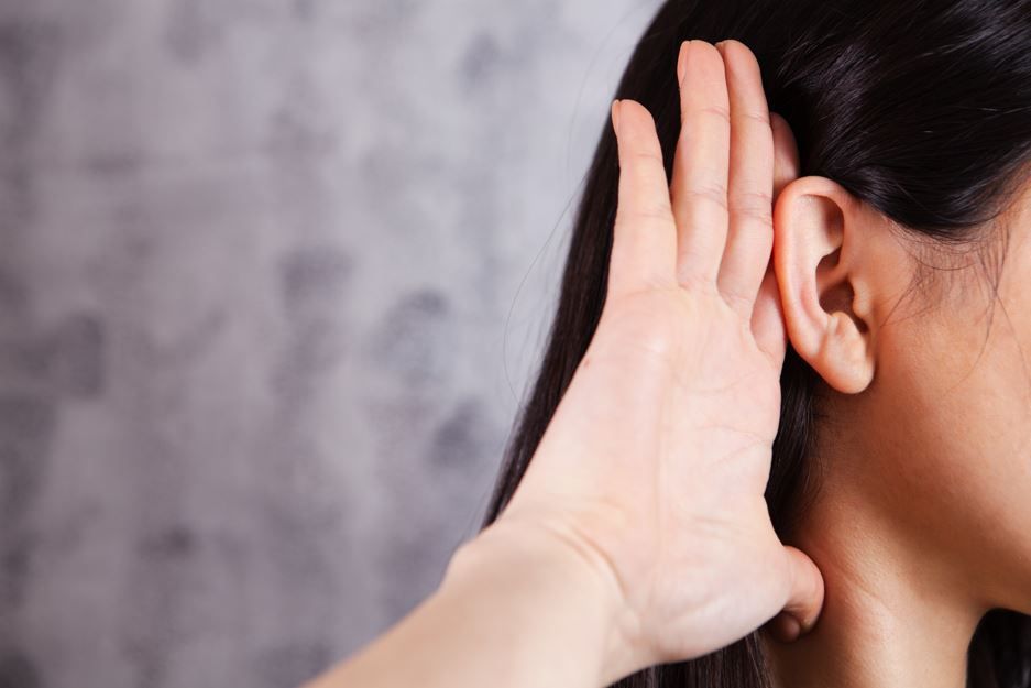 Mujer con la mano ahuecada detrás de la oreja, escuchando atentamente.
