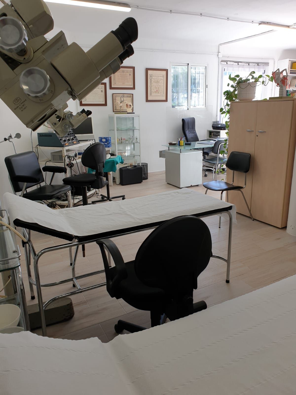 Interior de consultorio médico con camillas de exploración, equipos y mobiliario de oficina.