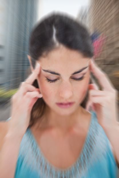 Mujer con los ojos cerrados, dedos en las sienes, fondo de paisaje urbano desenfocado.