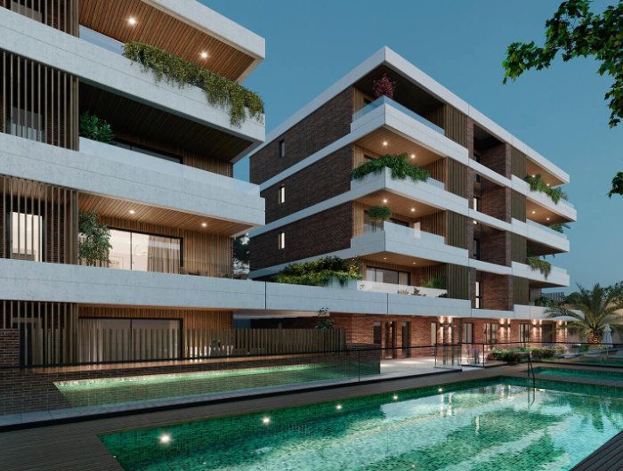 Edificio de apartamentos moderno con balcones junto a una piscina turquesa al atardecer.