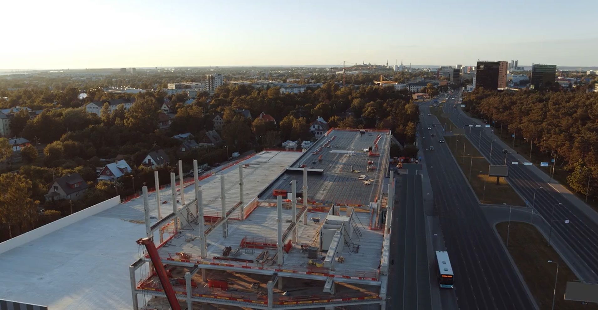 Vista aérea de una gran obra en construcción junto a una autopista al atardecer, con grúas y una estructura parcialmente construida.