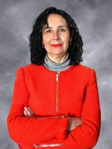 Mujer con chaqueta roja y brazos cruzados, sonriendo contra un fondo gris de estudio.
