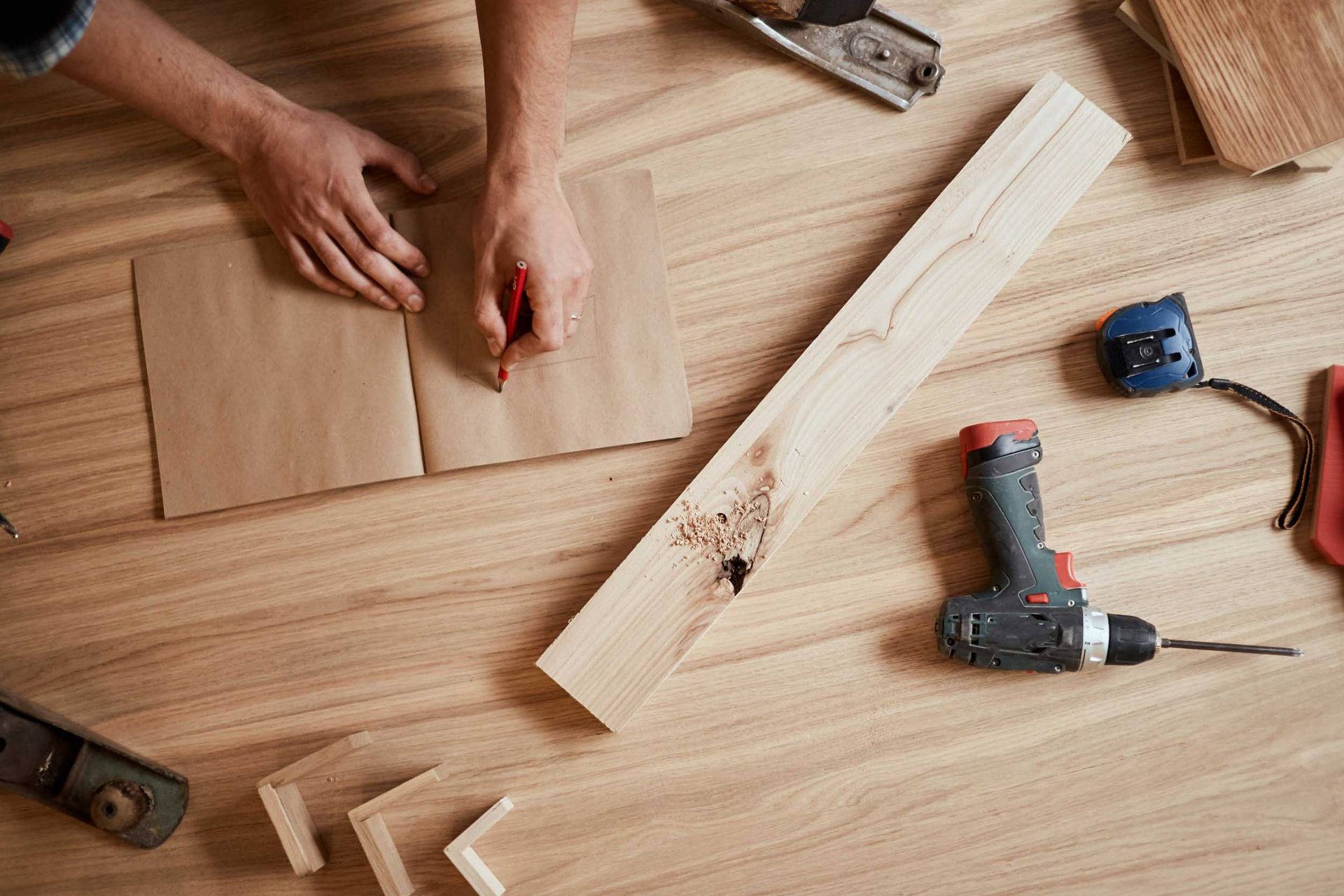 Persona dibujando en papel con madera, taladro y herramientas sobre superficie de madera.