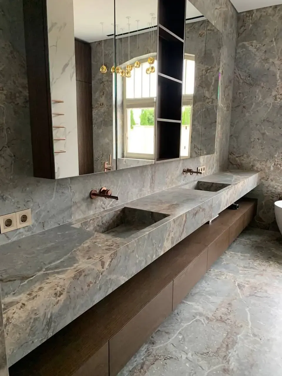 Tocador de baño moderno con encimera de mármol gris, dos lavabos y espejo en una pared alicatada.