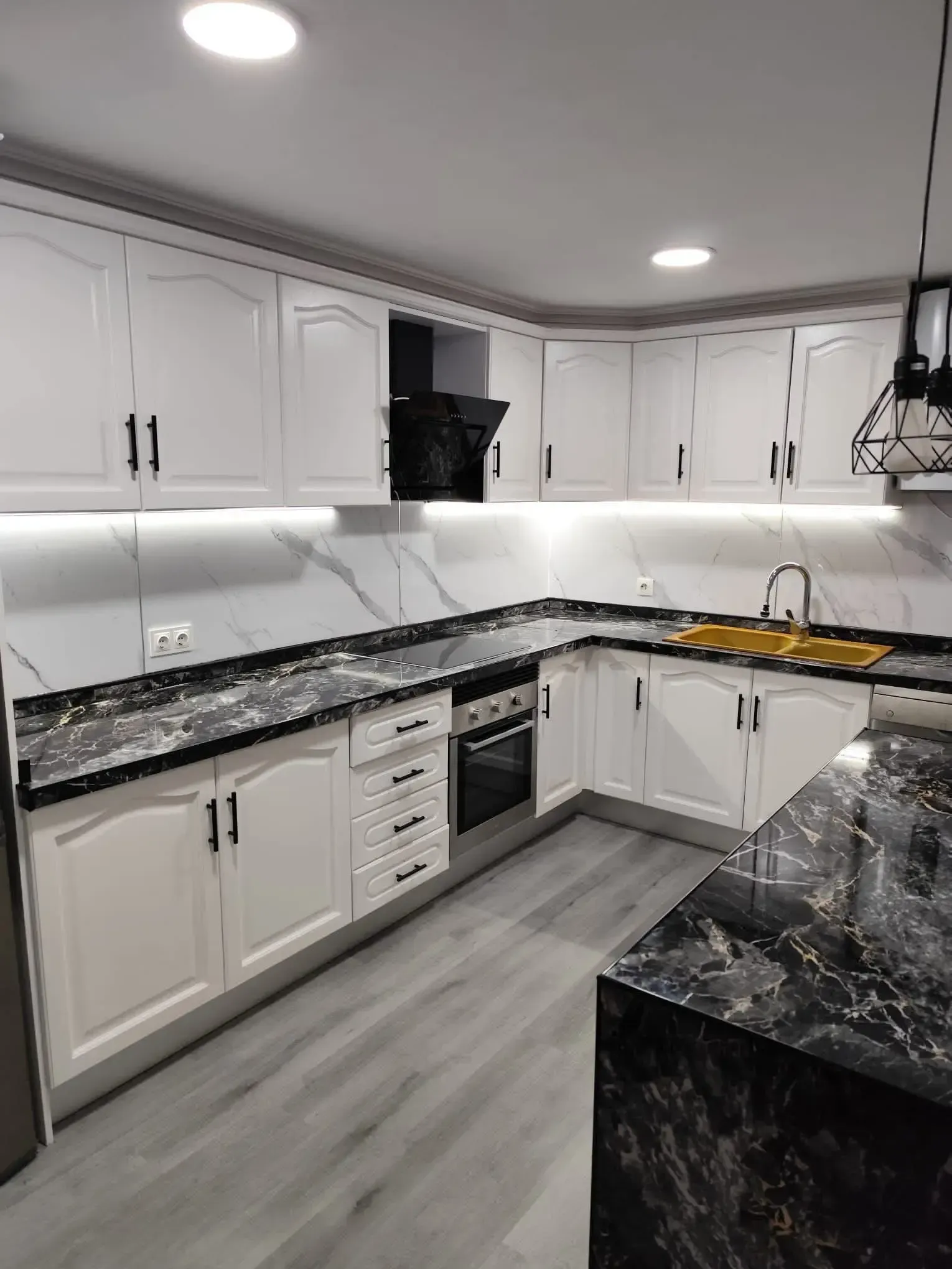 Cocina moderna blanca con encimeras de granito negro, suelo gris e iluminación bajo los armarios.
