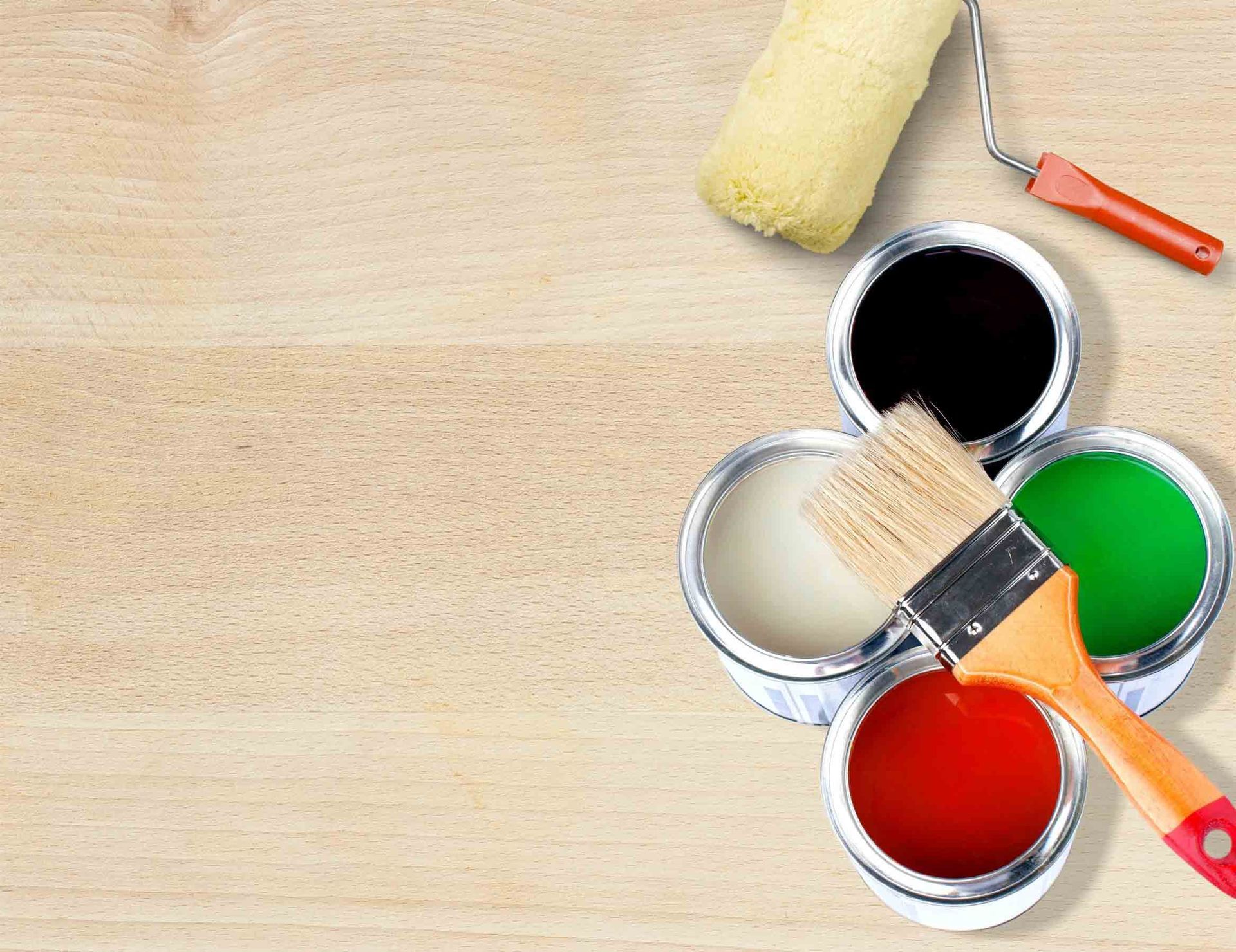 Latas de pintura con pintura negra, blanca, verde y roja, rodillo de pintura y pincel sobre superficie de madera.