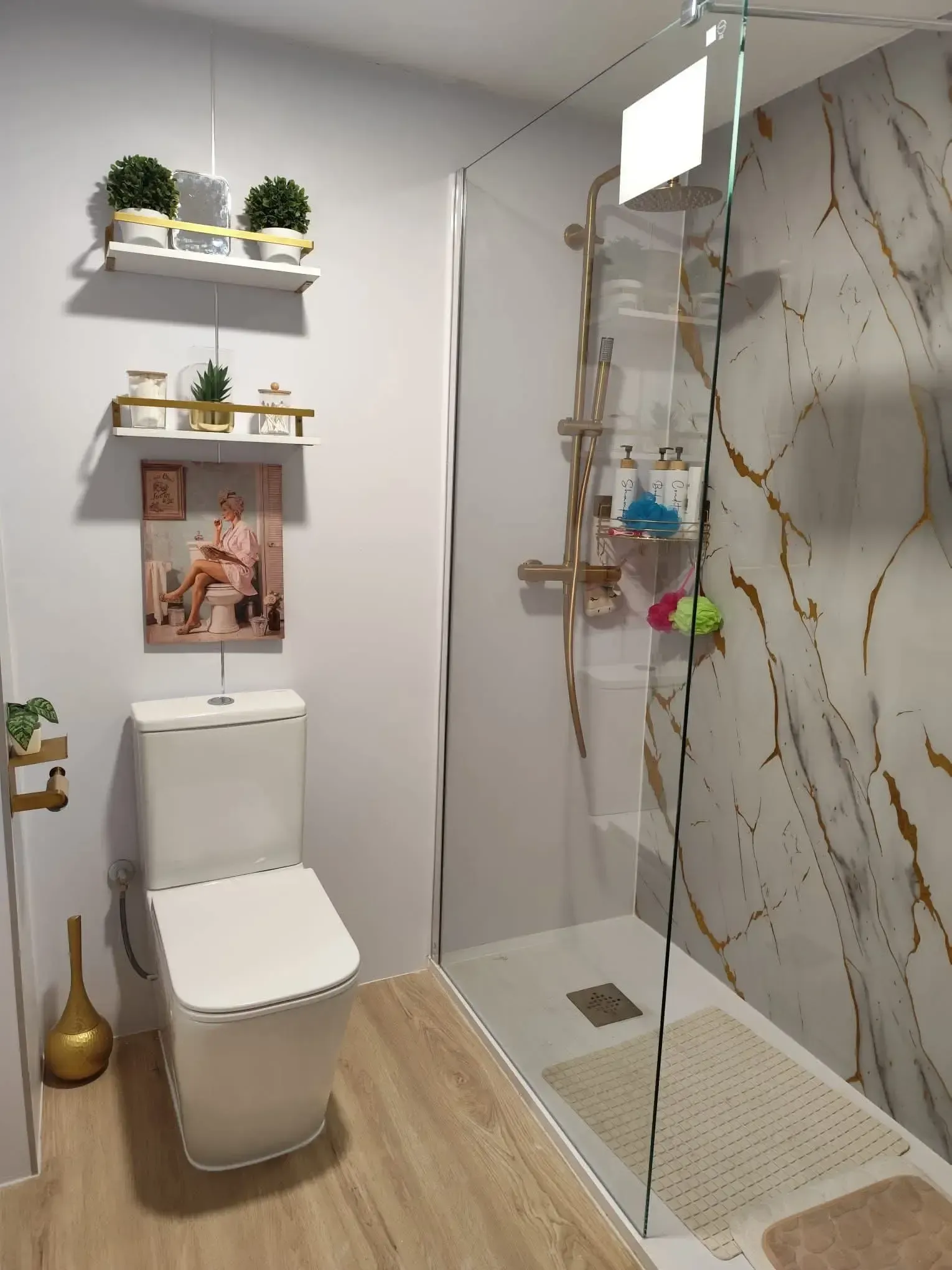 Baño moderno con inodoro, ducha de cristal, estantes de pared y suelo con aspecto de madera.