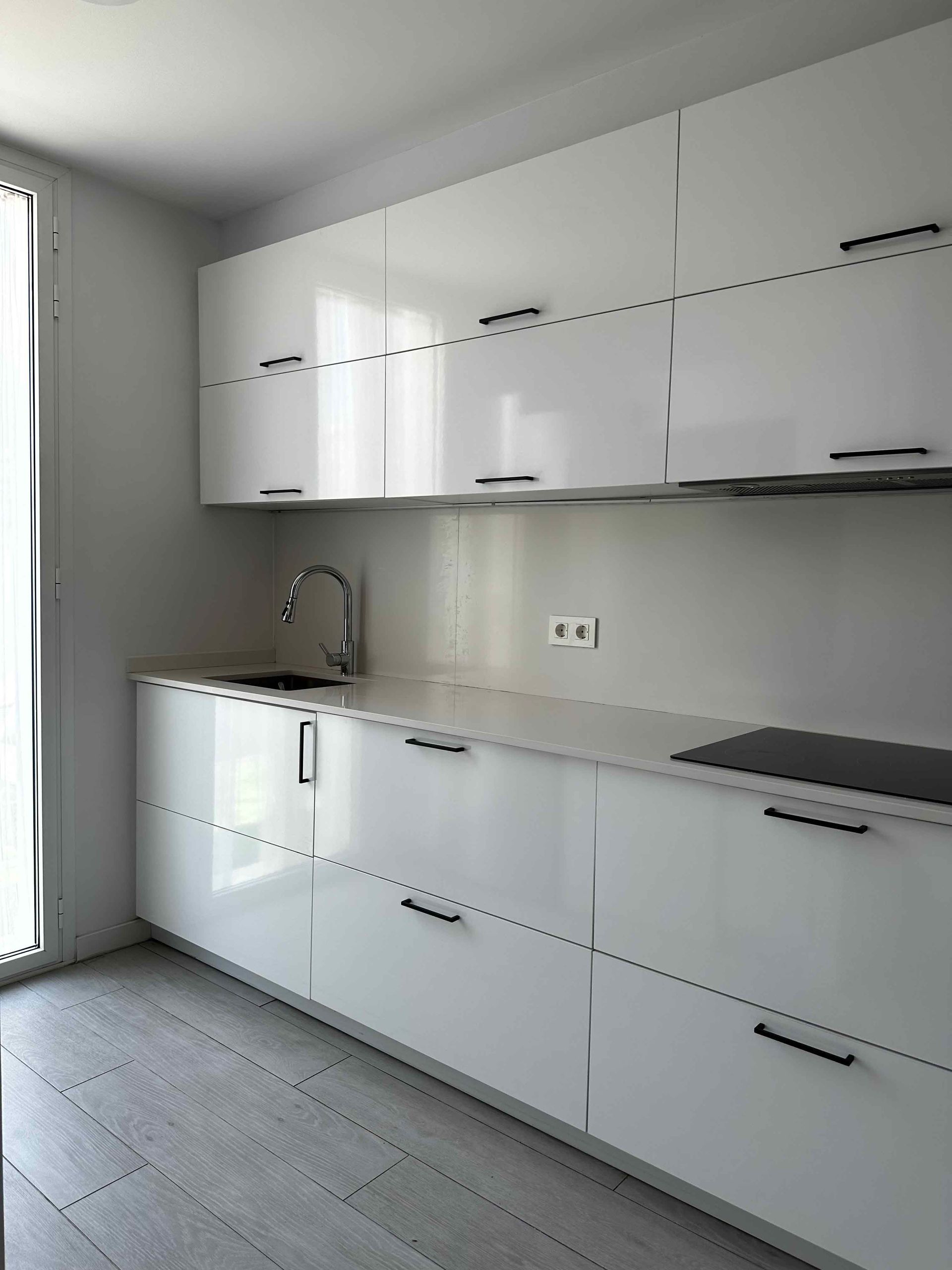 Cocina blanca moderna con gabinetes brillantes, encimera y fregadero.