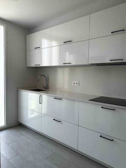 Cocina blanca moderna con gabinetes brillantes, encimera y fregadero.