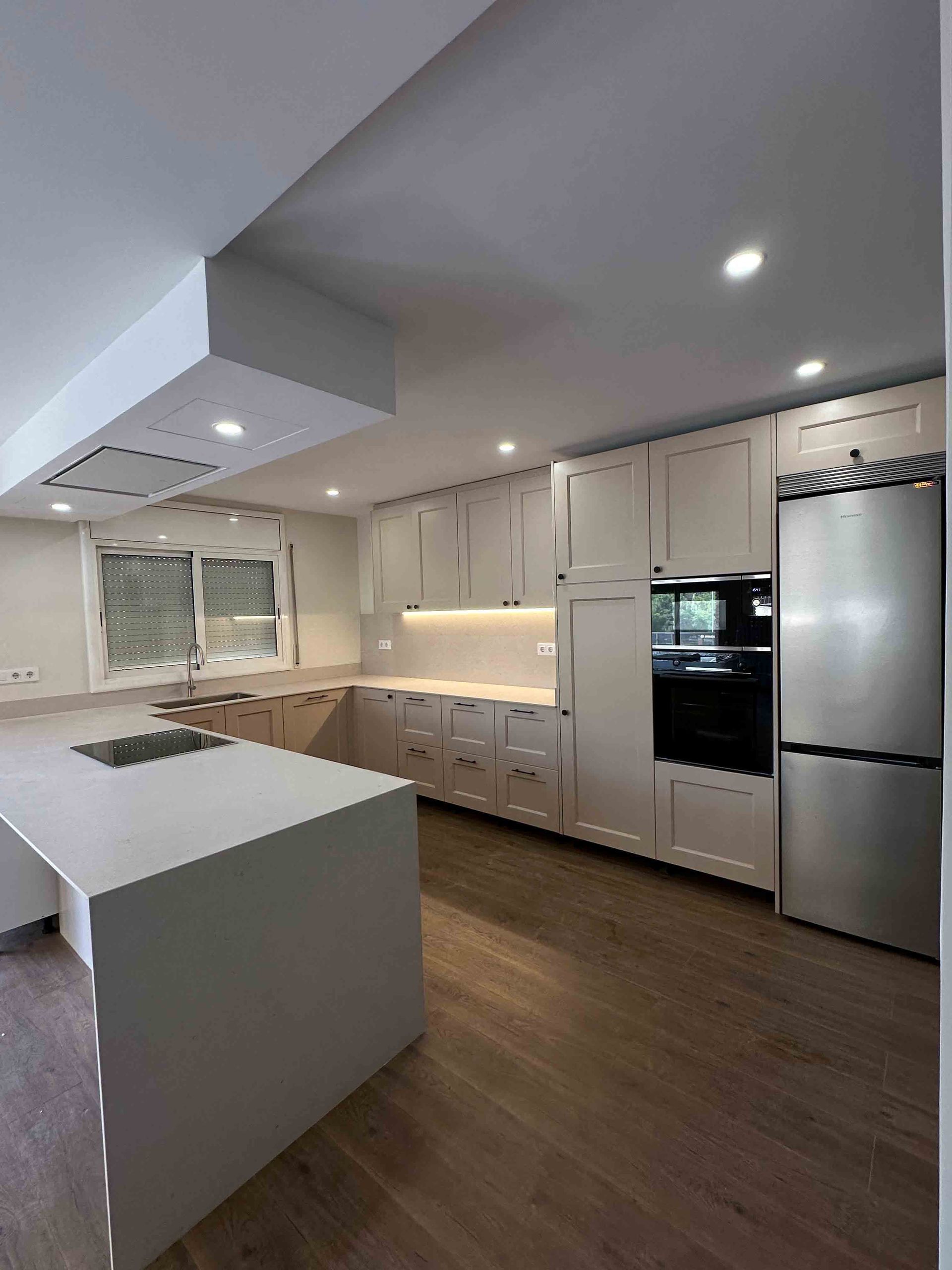 Cocina moderna con gabinetes color gris claro, isla, refrigerador de acero inoxidable y pisos de madera.