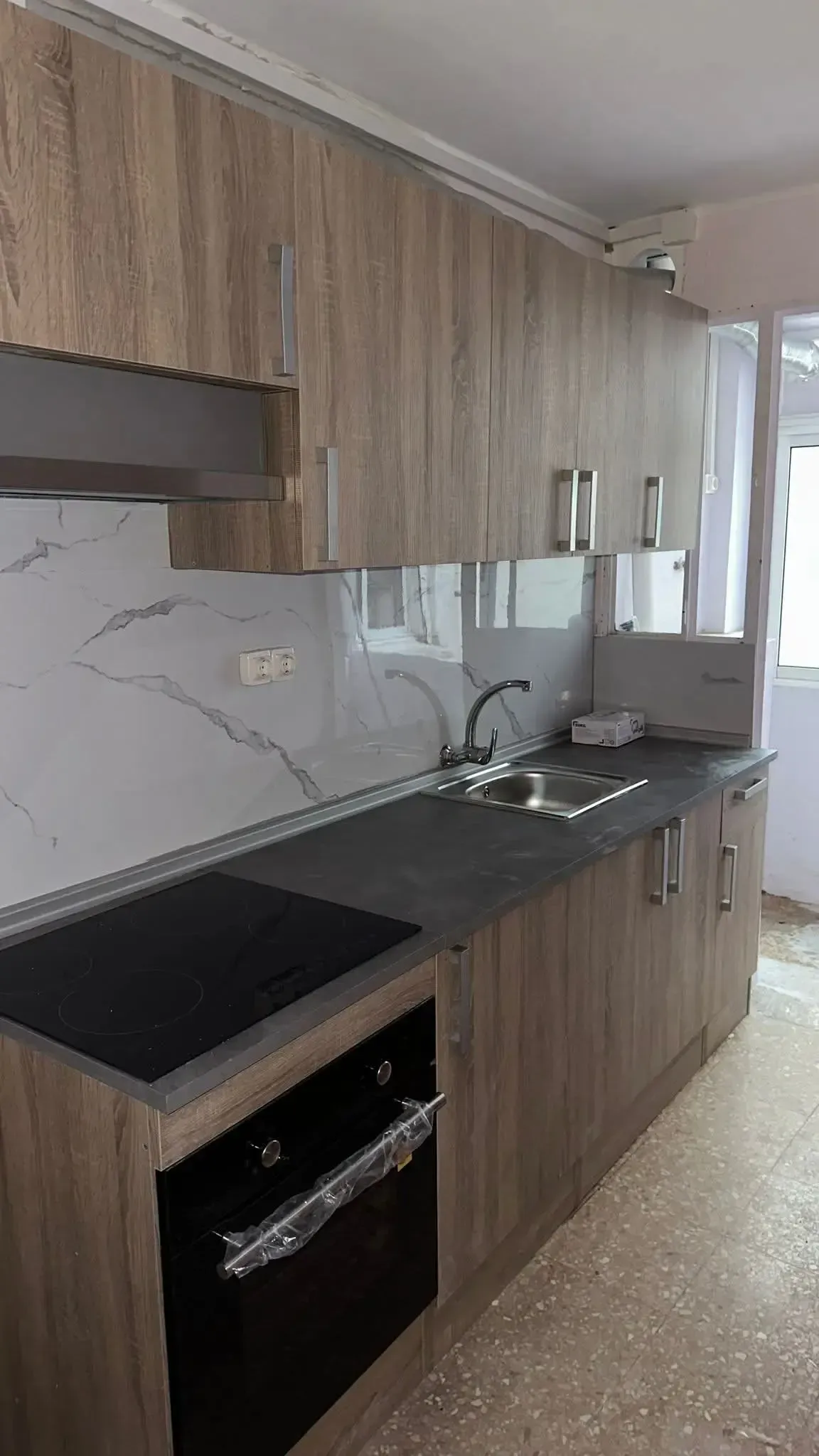 Cocina moderna con armarios de madera, encimera negra, salpicadero de mármol blanco y horno empotrado.