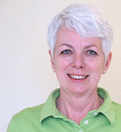 Eine Frau mit weißem Haar trägt ein grünes Hemd und lächelt.