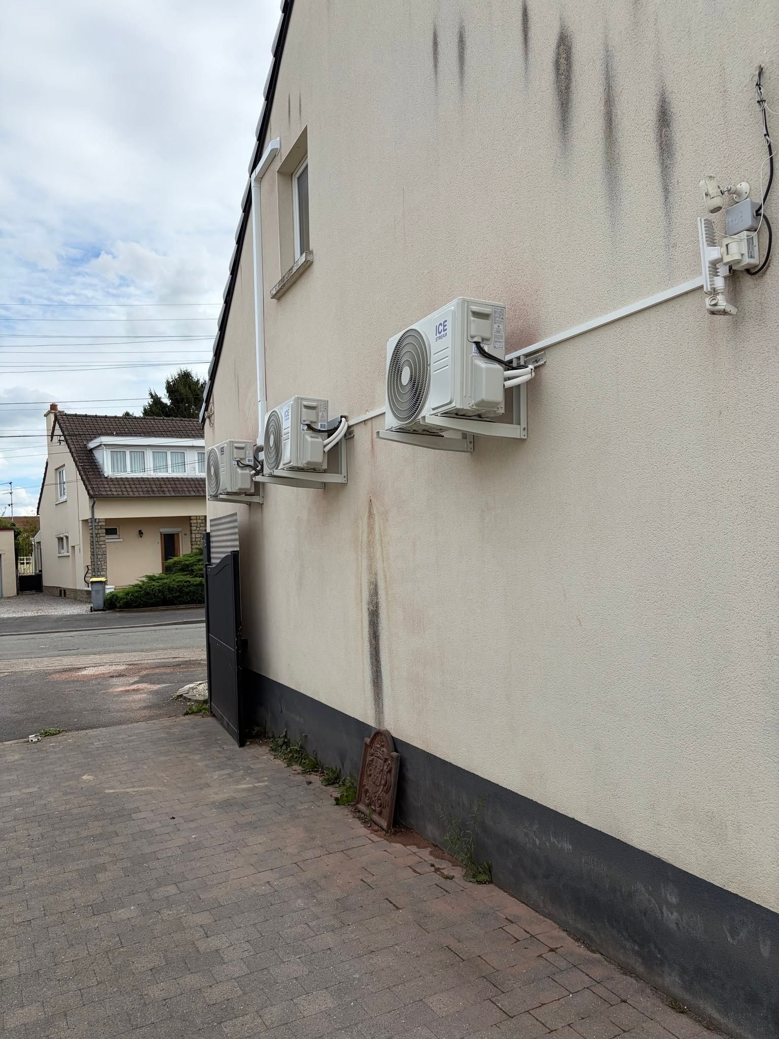 Côté d'un bâtiment beige avec des climatiseurs et des gaines installés à côté d'une ruelle pavée.
