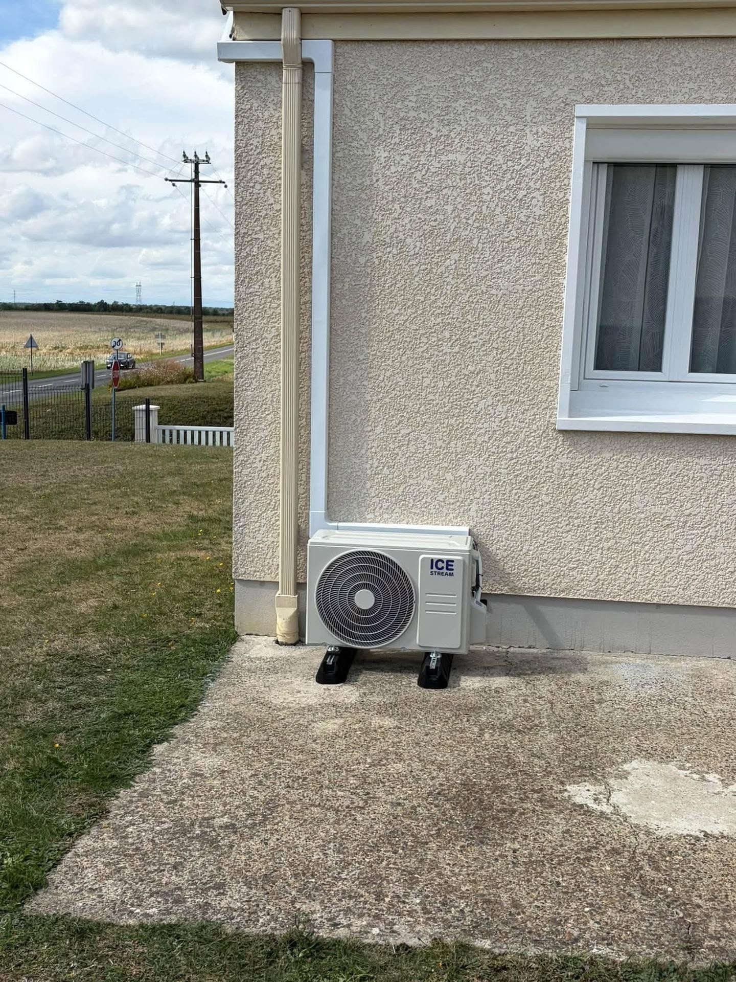 Mur extérieur d'une maison avec un petit climatiseur extérieur à côté d'un chemin en béton.