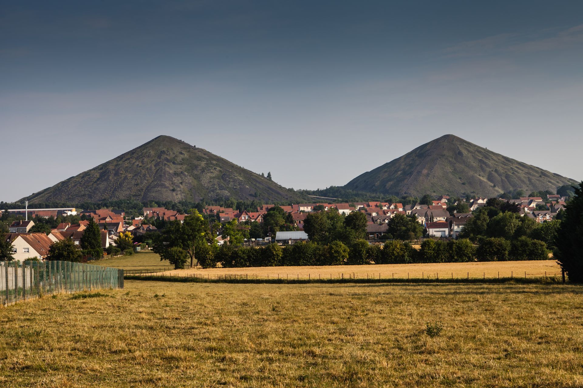 Deux collines derrière un village et un champ doré sous un ciel bleu clair