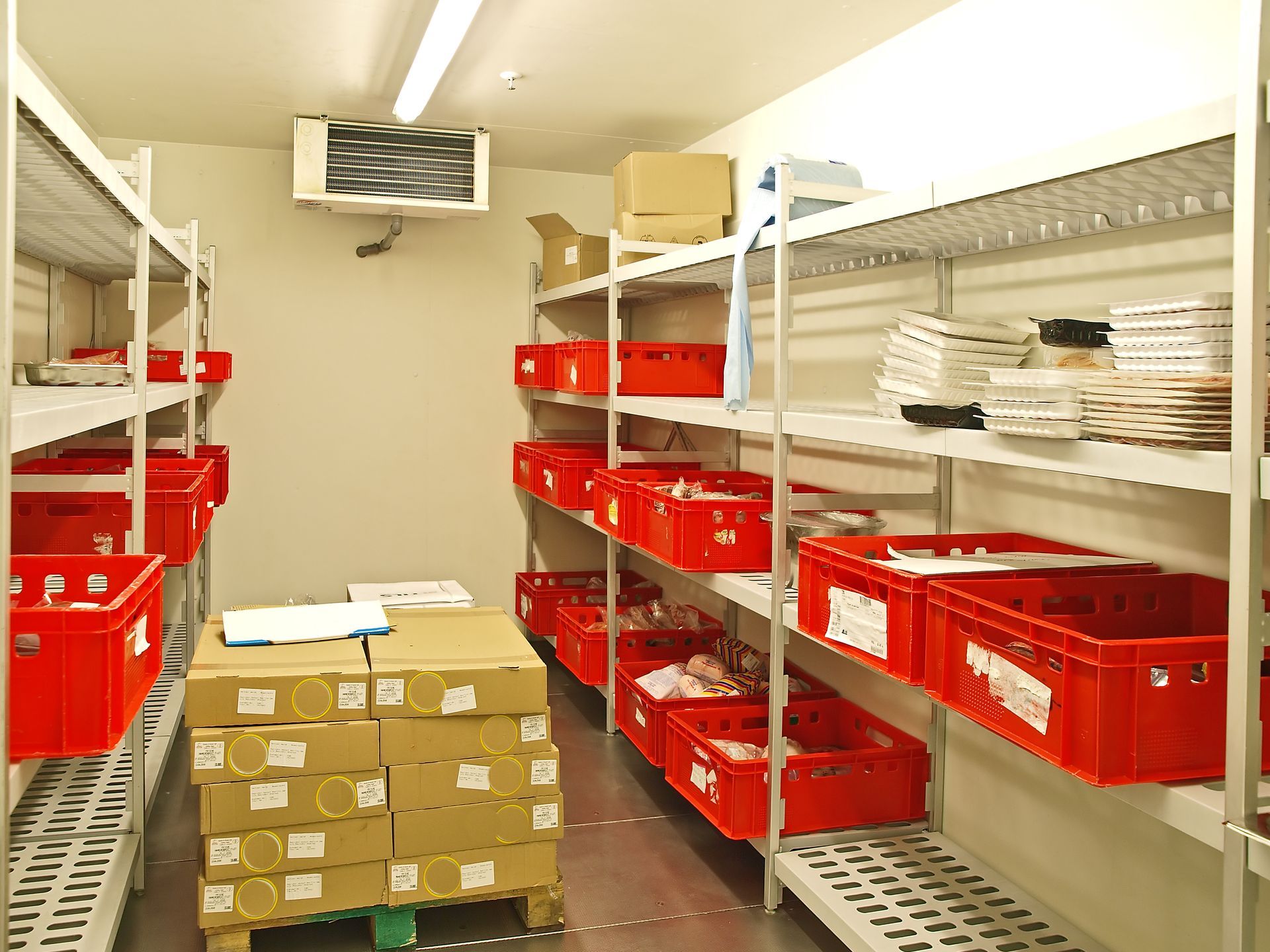 Pièce de stockage avec des bacs rouges, des cartons empilés et des étagères sous une lumière vive.
