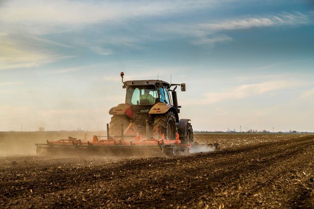 Un tracteur laboure un champ poussiéreux sous un ciel nuageux