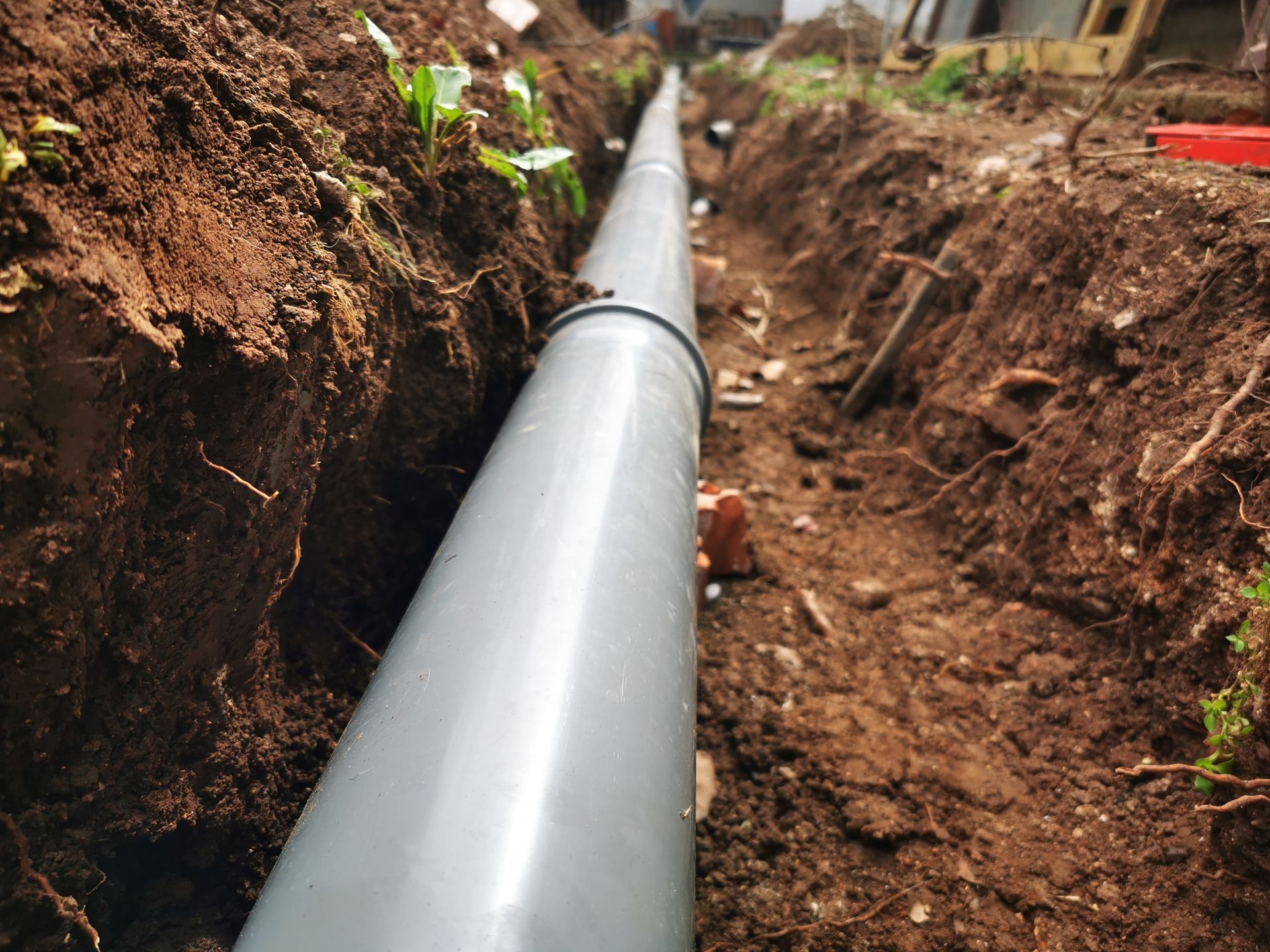 Un tuyau gris a été posé dans une tranchée de terre lors de la construction, avec de la terre empilée des deux côtés.