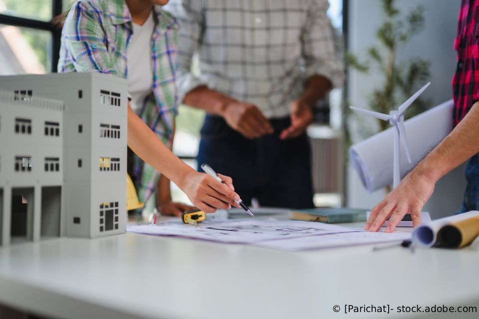 Menschen arbeiten in einer Bürobesprechung neben einem Gebäudemodell an Architekturplänen.