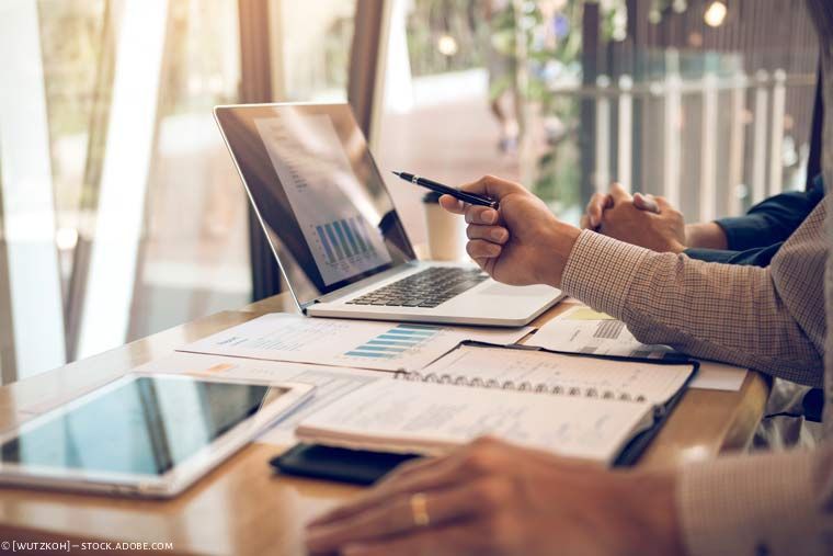 Personen, die an einem Schreibtisch mit Laptop und Tablet Finanzdiagramme und Dokumente prüfen.