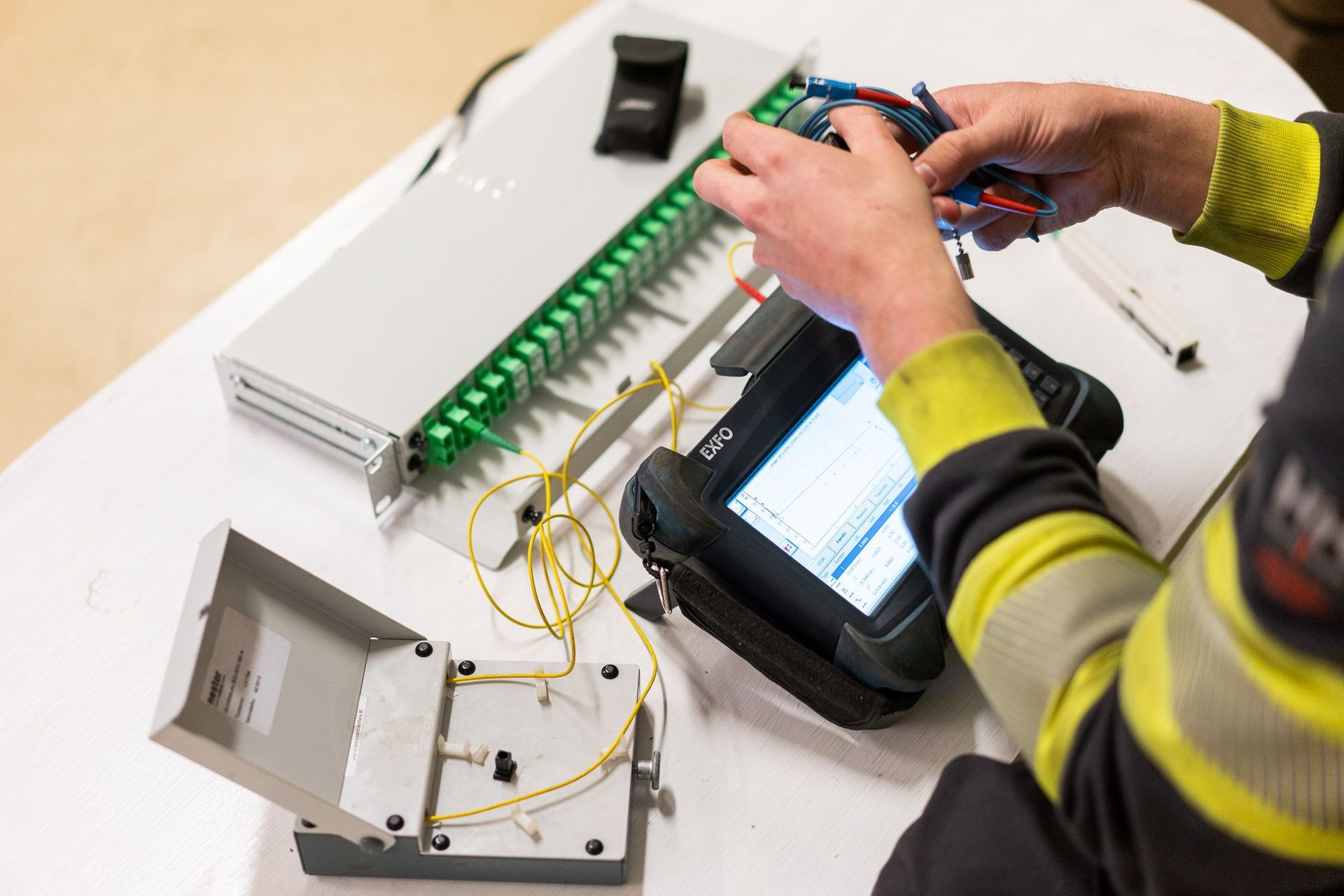 Teknikko kytkee sähköohjauspaneelia tabletin ja avoimen elektroniikkakotelon avulla työpöydällä.