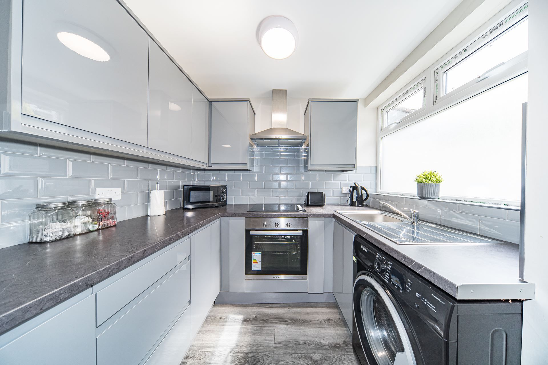 A kitchen with a washing machine , oven , sink , and microwave.
