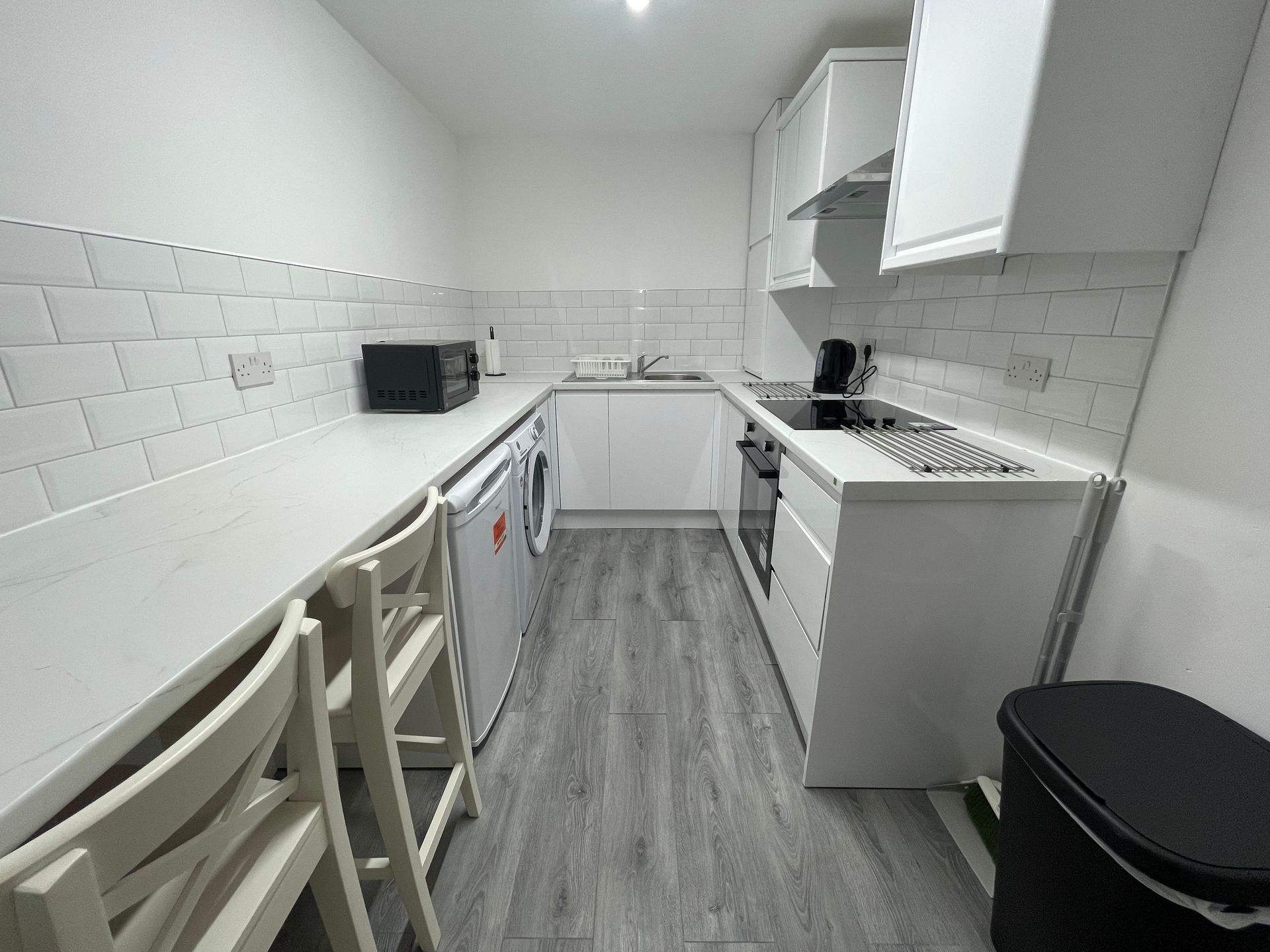 A kitchen with white cabinets , a stove , a microwave , and a trash can.