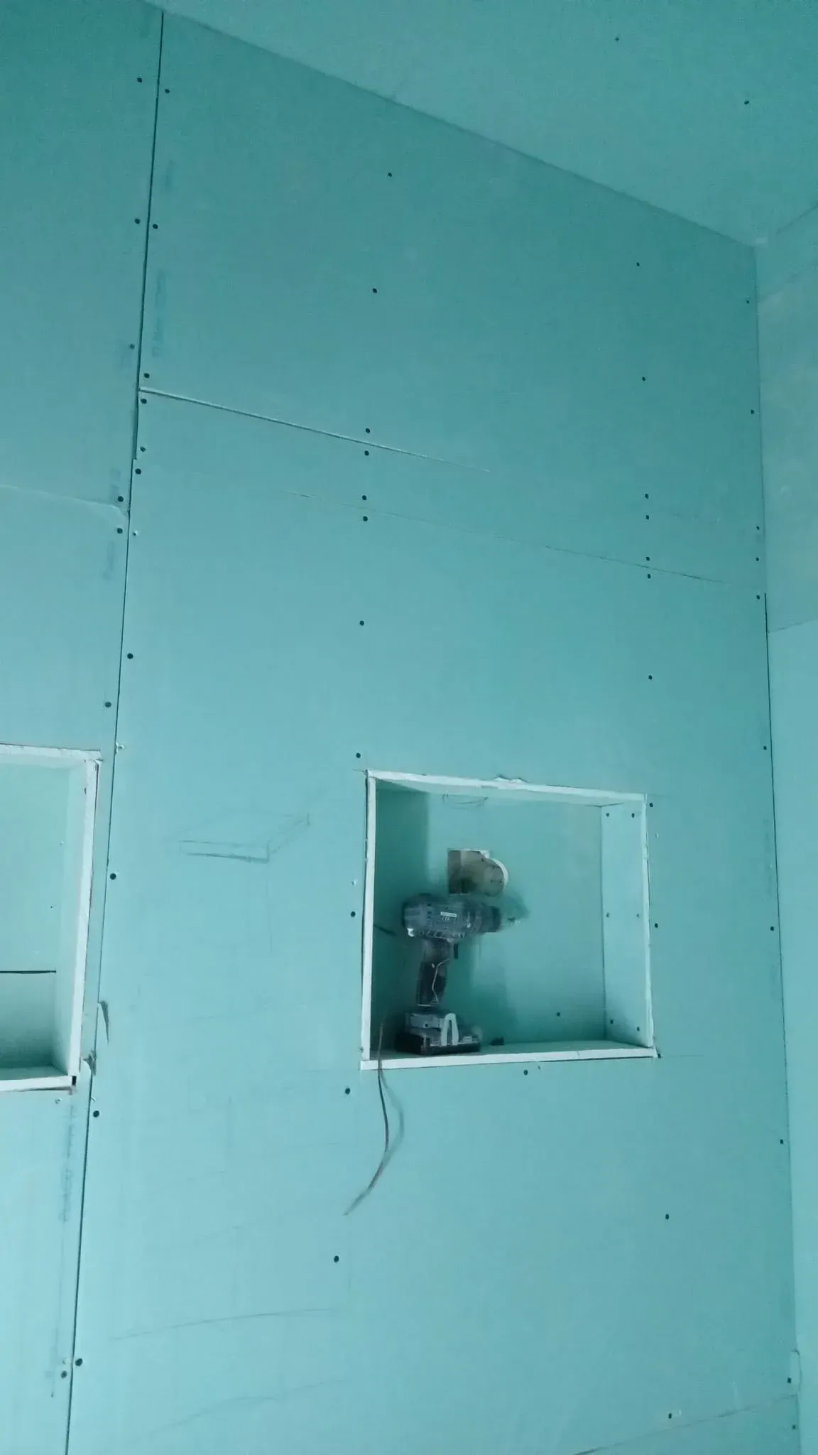 Pared de pladur color verde azulado con recortes cuadrados para instalaciones eléctricas en construcción.