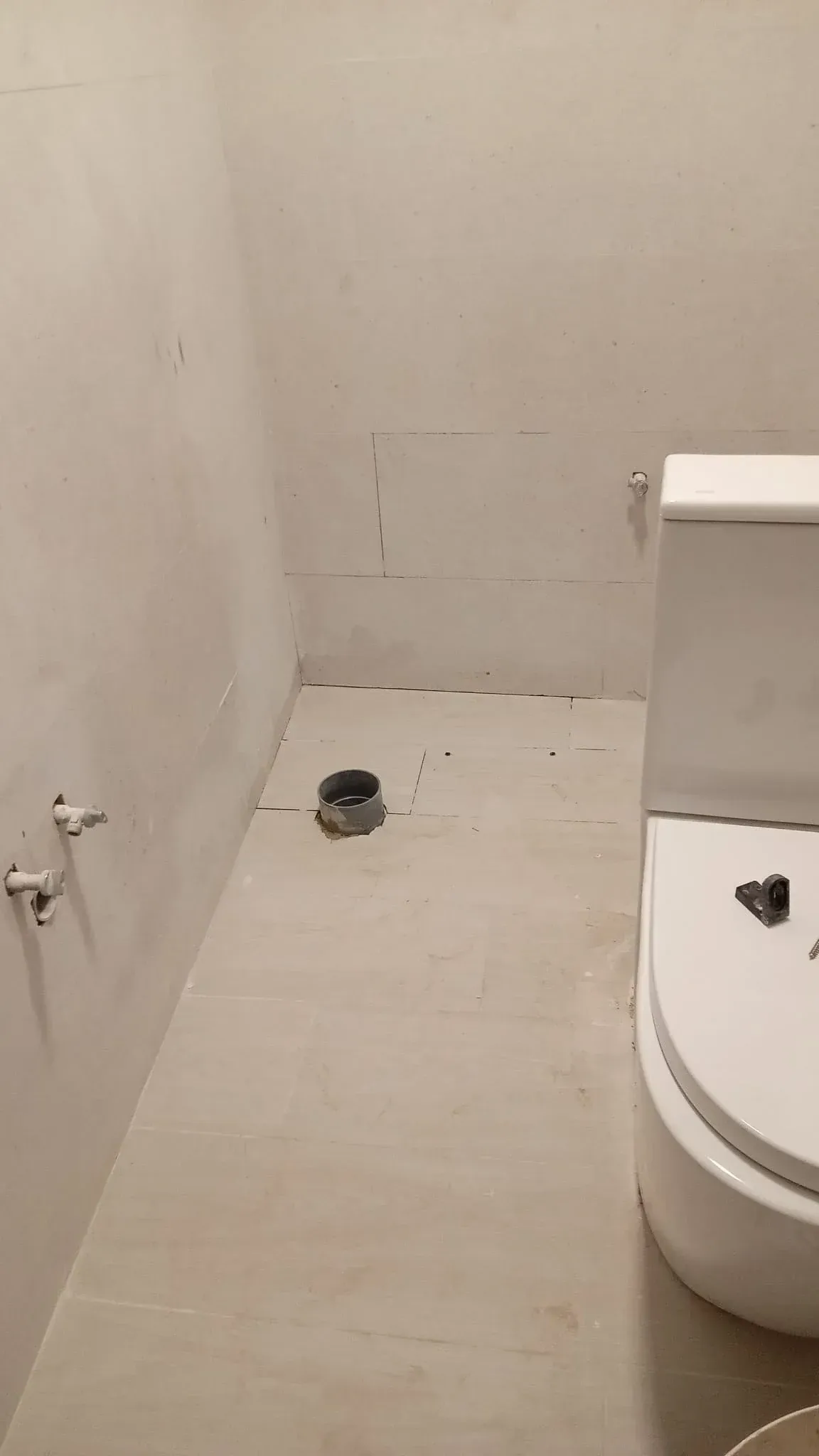 Baño pequeño sin terminar con inodoro, paredes desnudas y desagüe en el suelo.