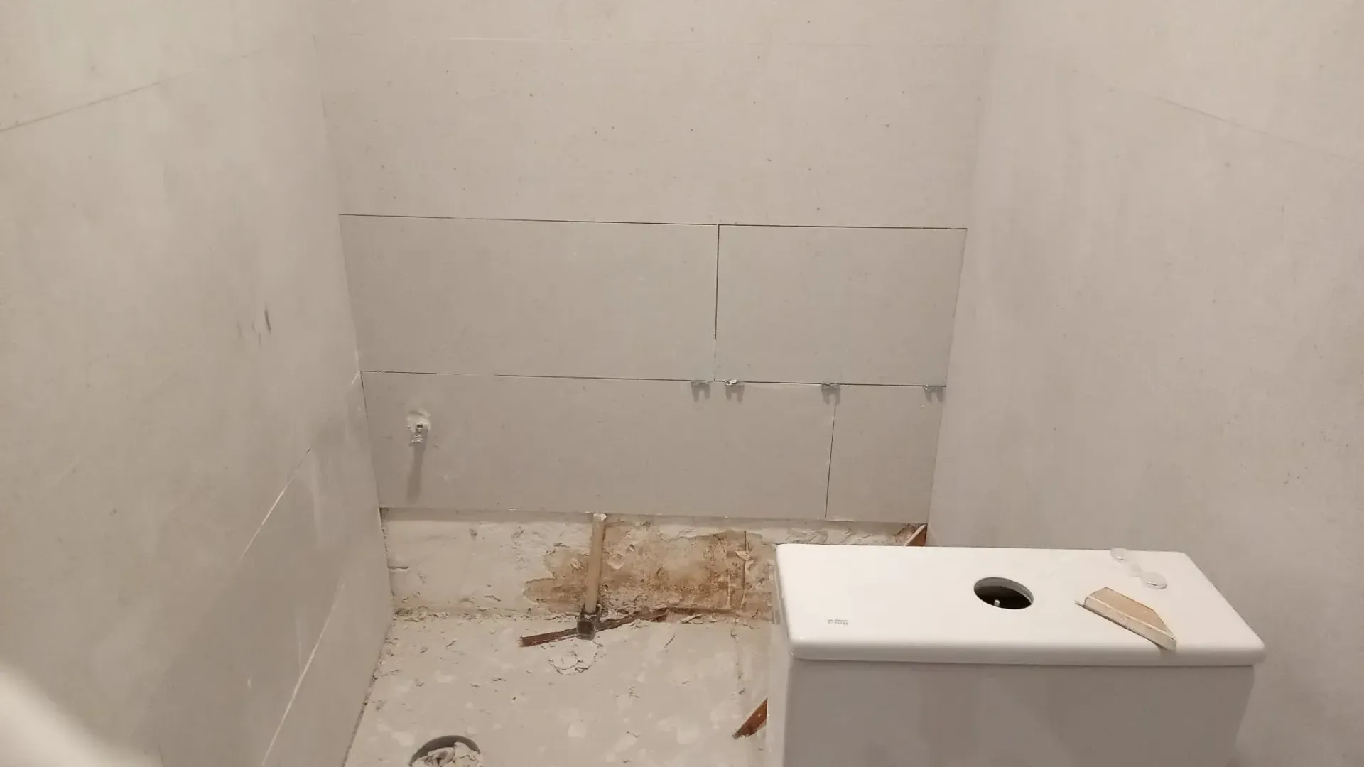 Pequeño baño vacío en construcción con escombros en el suelo y un lavabo o mostrador blanco en primer plano.