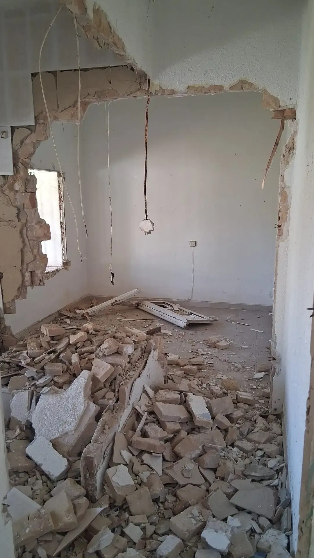 Habitación parcialmente demolida con escombros en el suelo y paredes y techo dañados al descubierto.