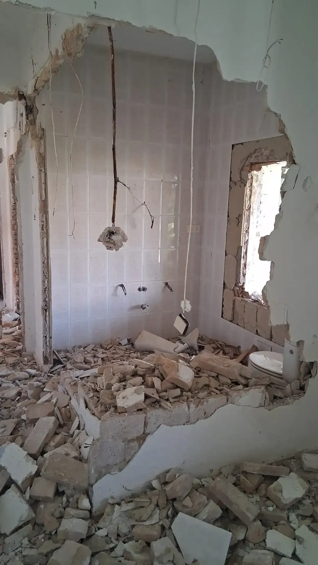 Habitación en demolición con escombros en el suelo y una pared dañada con una ventana abierta.