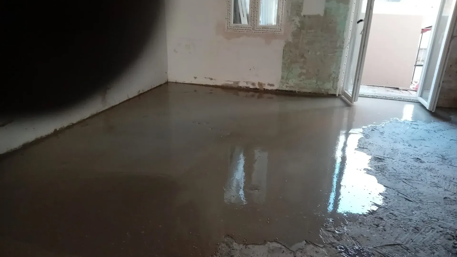 Habitación inundada con agua estancada y una pared dañada cerca de una puerta abierta.