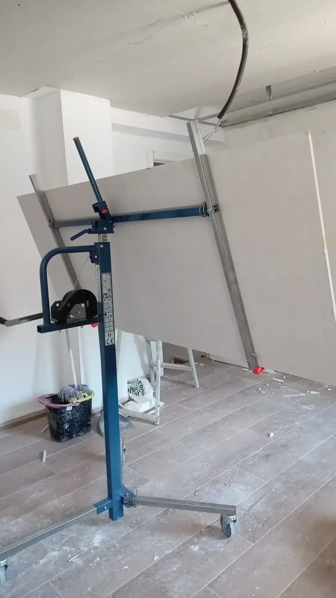 Paneles de yeso azules levantados en una habitación parcialmente terminada con paredes blancas y suelo a la vista.
