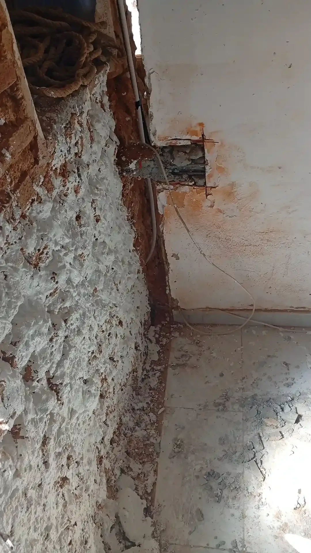 Pared interior dañada con yeso desconchado, cableado expuesto y una ventana luminosa debajo.
