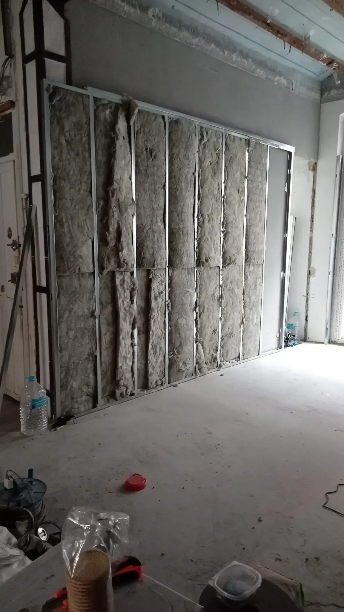 Pared interior parcialmente terminada con paneles de aislamiento a la vista en una habitación polvorienta.