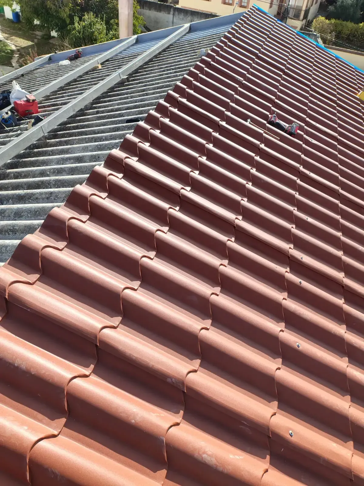 Persona con chaleco amarillo en un tejado, utilizando un taladro en las tejas. Cielo azul al fondo.