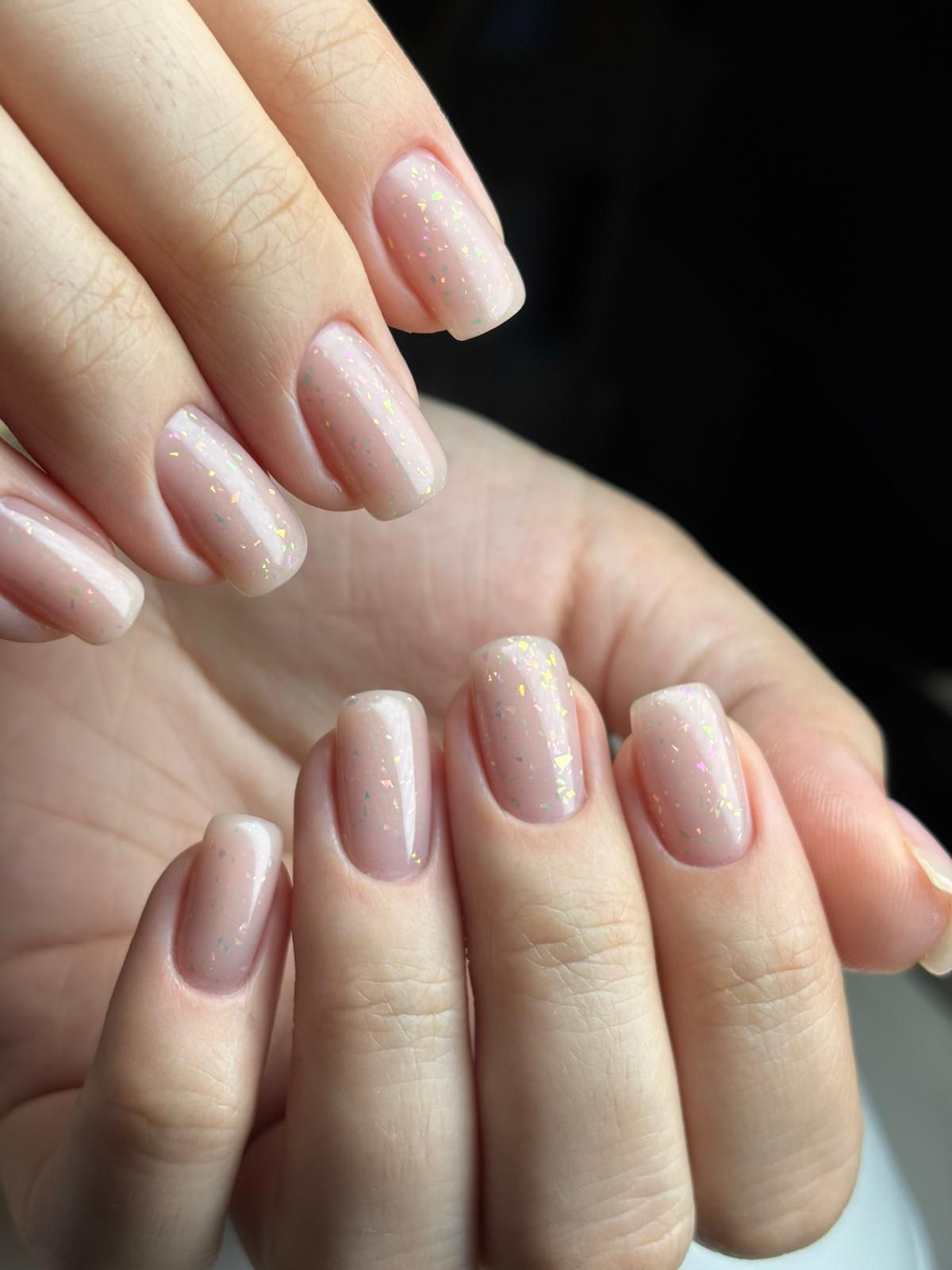 Primer plano de manos con uñas cuadradas de color rosa claro y brillantes.