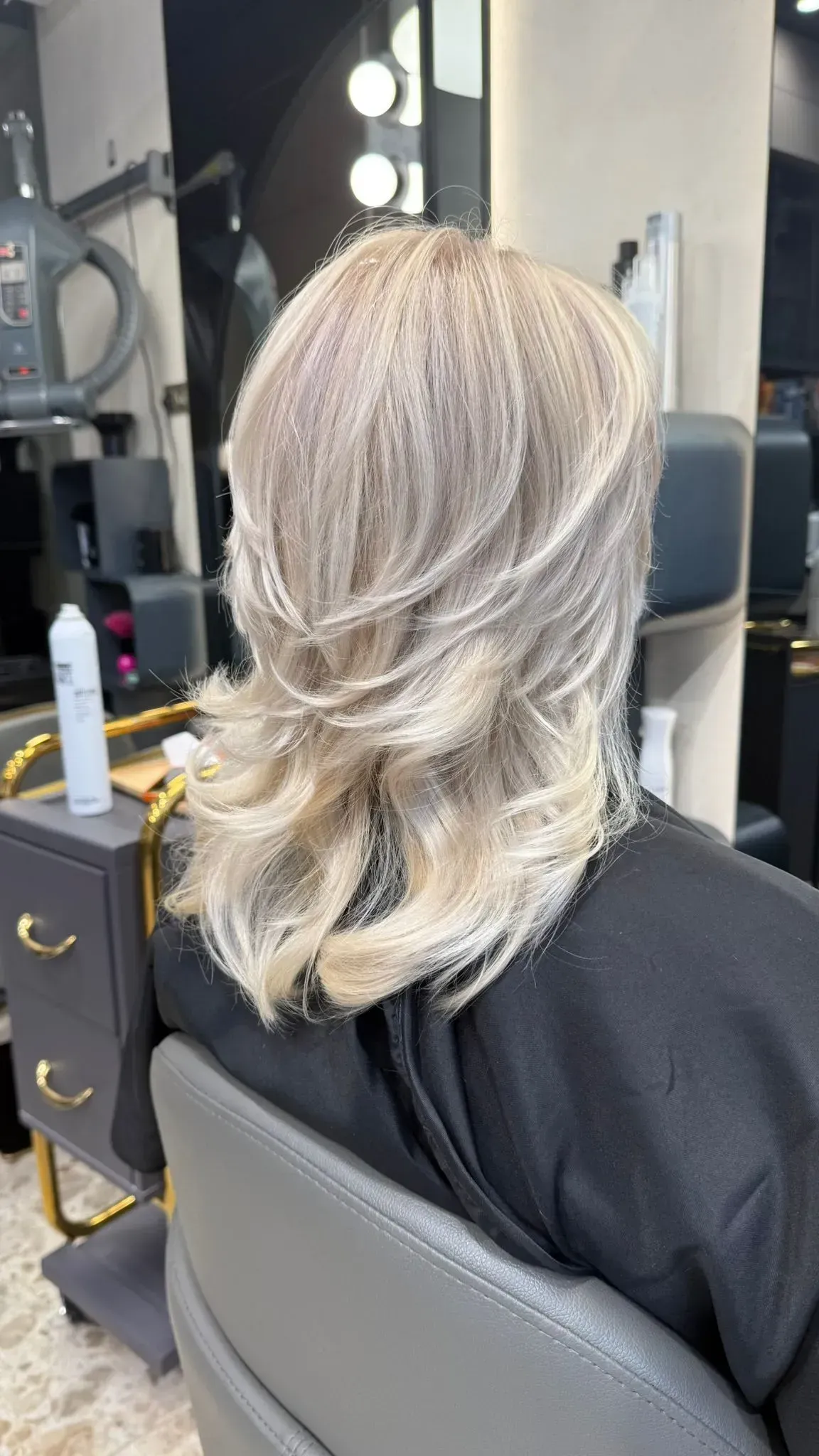 Cabello rubio peinado en capas, vista posterior. Persona sentada en una silla de peluquería.